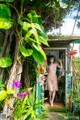 A woman standing in the doorway of a house surrounded by plants.