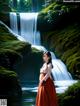 A woman standing in front of a waterfall in a forest.