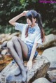 A young woman sitting on a rock by a stream.