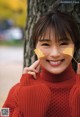 A woman in a red sweater holding a leaf in her hand.