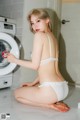 A woman in a white lingerie sitting on the floor next to a washing machine.